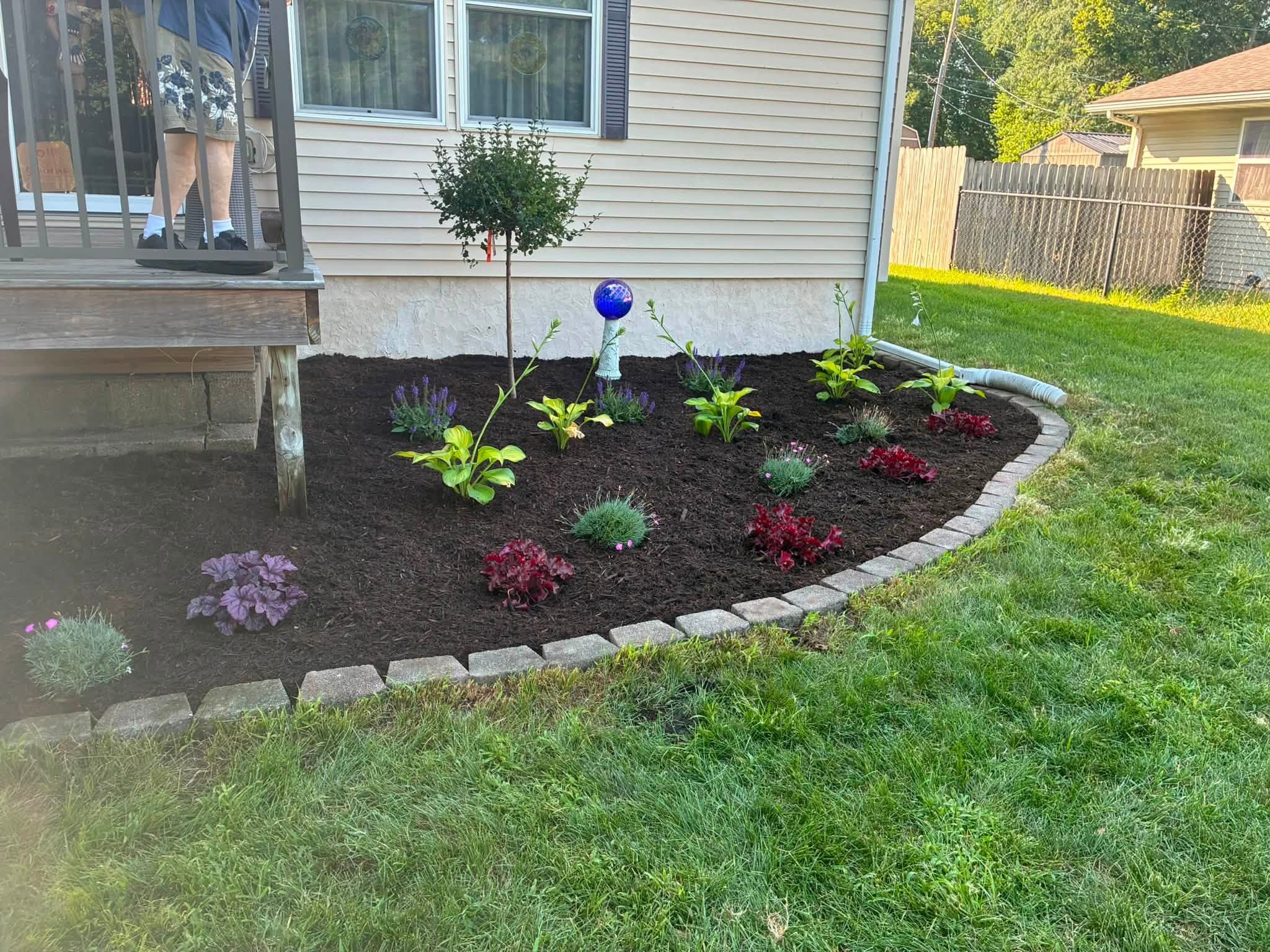 After: refreshed mulch, colorful plants, and curved stone edging beside the same porch
